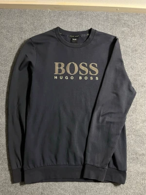 BOSS Hugo Boss – Dark Blue Sweatshirt (M) - Classic and refined BOSS Hugo Boss sweatshirt in deep navy blue. Size M, length 68 cm, width 48 cm – a comfortable and sleek fit for everyday wear. The front features the bold BOSS HUGO BOSS logo in elegant metallic print, giving it a premium and timeless look.  ✅ Condition: Good 💯 Authenticity: 100% genuine, verified by the original Hugo Boss label 📦 Shipping: Dispatched immediately after purchase – fast and reliable delivery!  This sweatshirt combines Hugo Boss’s signature minimalist design