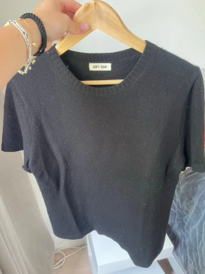 Svart stickad t-shirt Soft Goat - En svart stickad t-shirt från Soft Goat med rund halsringning och korta ärmar. Tröjan har en enkel och clean design, perfekt för att styla med jeans eller kjol. Materialet känns mjukt och lyxigt, och passformen är normal.