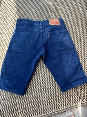 Blå jeansshorts från Levi's - Snygga blå jeansshorts från Levi's med klassisk femficksdesign och subtilt mönster i tyget. Shorts med normal midja, bälteshällor och Levi's ikoniska läderpatch bak. Perfekta för en avslappnad stil i sommar.