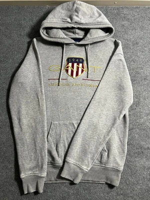 GANT – Grey Hoodie (S) - Classic and comfortable GANT hoodie in light grey. Size S, length 65 cm, width 51 cm – a perfect fit for a relaxed yet stylish look. The chest features the signature GANT 1949 American Sportswear logo with embroidered shield detailing, giving it that timeless preppy aesthetic.  ✅ Condition: Excellent – no wear, no stains 💯 Authenticity: 100% genuine, original GANT branding 📦 Shipping: Sent immediately after purchase – fast and reliable delivery!  This hoodie combines GANT’s premium craftsmanship