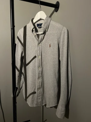 Ralph Lauren Skjorta  - Säljer en stilren grå Ralph Lauren skjorta i jätte bra skick. Skjortan är i storlek M men passar absolut folk med storlek S, modellen är 183cm lång och väger 66kg. Om du har några funderingar är det bara att höra av dig!