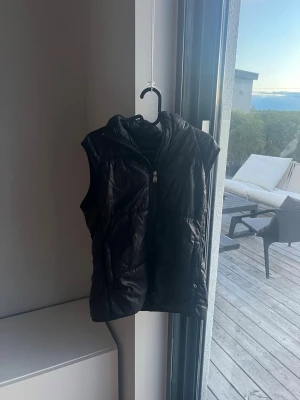 Svart dunväst  - Snygg svart dunväst med dragkedja . Västen har två stora fickor framtill och quiltad design. Perfekt för lager-på-lager och ger en cool look till din outfit. Passar dig som gillar streetstyle och vill hålla värmen utan att tumma på stilen. Original pris 3700