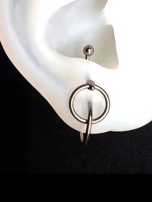 Unik Anti-tragus titan  - Unikt anti-tragus piercingskycke med två sammankopplade ringar i titan. Ena ringen är "lös" och kan användas till annan piercing om man vill. Helt ny och oanvänd. Banana Barbell 1.2 ×10 MM. Ring 1.2×8 MM. Nickelfritt och allergivänligt.