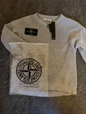 Ljusgrå stickad tröja Stone Island - Ljusgrå stickad tröja från Stone Island med klassisk rund halsringning och ribbade muddar. Kommer med orginal påse och tags, endast använd 1 gång och är i väldigt fint skick. Vid fler funderingar mm, skriv ett meddelande.