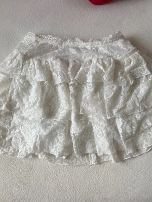 Vit volangkjol i spets - Supersöt vit kortkjol med inbyggda shorts med flera volanger i spetsmaterial. 