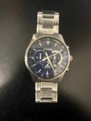 Citizen herrklocka med blå urtavla - Stilren herrklocka från Citizen med blå urtavla och flera små urtavlor. Klockan har ett klassiskt armband i silverfärgat metall och rund boett. Perfekt accessoar för dig som gillar en tidlös och modern look.