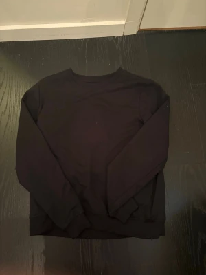Svart sweatshirt från OTP - En stilren svart sweatshirt från OTP, tillverkad i mjukt material med rund halsringning och ribbade muddar vid ärmslut och nederkant. Perfekt för en avslappnad och enkel look. Passar till det mesta och är lätt att matcha med andra plagg.