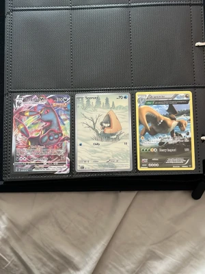 Pokémonkort samling i pärm - (🎈Bud på dessa pokemon kort skriv ifall ni är intresserade hjälper till med allt🎈)Säljer en samling Pokémonkort i pärm, med flera holografiska och specialkort som Umbreon VMAX, Dragonite och Greninja GX. Kort i olika färger och motiv, med både klassiska och moderna Pokémon. Perfekt för samlare eller fans av Pokémon.