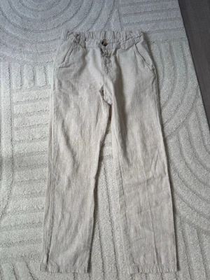 Beiga linnebyxor från Kappahl - Snygga beiga linnebyxor från Kappahl. Byxorna har raka ben och sidfickor, perfekta för en avslappnad och stilren look. Tillverkade i ett luftigt linnematerial som passar bra till varmare dagar.