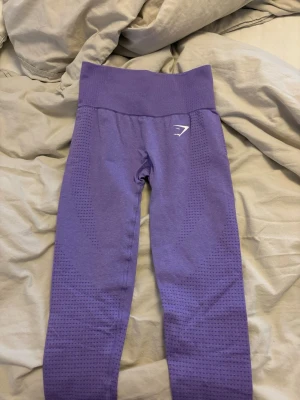 Lila seamless leggings från Gymshark - Snygga lila seamless leggings från Gymshark med hög midja och diskret mönster längs benen. Stretchigt material som sitter tajt och bekvämt. Perfekta för träning eller chill. Gymshark-logga i vitt på höften.