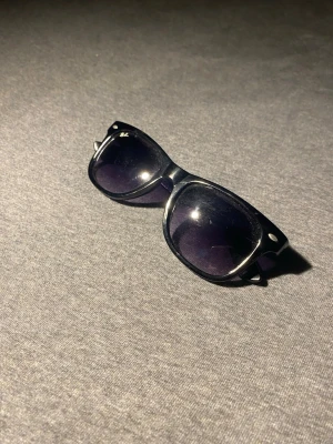 Svarta solglasögon - Snygga svarta solglasögon med bred båge och mörka glas. Klassisk design med lätt rundade kanter och små silvriga detaljer vid sidorna. Perfekta för att ge en cool vibe till din outfit. UV-skydd enligt märkning på insidan av skalmen.