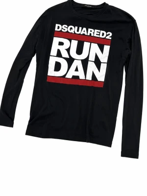 Svart långärmad t-shirt Dsquared2 - ( armarna ser väldigt små ut på bilderna men det är för dom viker sig när man lägger ner tröjan) Cool svart långärmad t-shirt från Dsquared2 med stort vitt och rött tryck på framsidan där det står 'RUN DAN'. Skön passform och tillverkad i mjuk bomull. Perfekt för dig som gillar streetwear och vill sticka ut med ett statement-plagg.