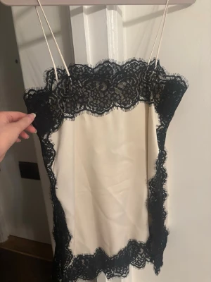 Krämfärgad linne  med svart spets från Zara  - Snyggt linne  i krämfärgat tyg med tunna axelband och dekorativa svarta spetsdetaljer längs kanterna. Perfekt för att skapa en chic och feminin look. Materialet känns mjukt och följsamt mot huden. Virala linnet från Zara 
