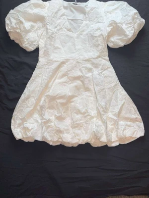 Vit kort klänning med puffärmar - Superfin vit kort klänning med puffiga ärmar och v-ringning. Klänningen har även broderade blommor i tyget 