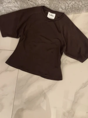 Brun t-shirt från Pull&Bear - Mörkbrun t-shirt från Pull&Bear med rund halsringning och korta ärmar. Enkel och stilren modell i mjukt bomullsmaterial, perfekt att matcha med jeans eller kjol.