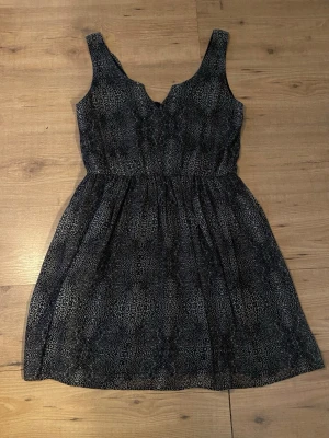 Svart kortklänning med leopardmönster - Snygg svart kortklänning med leopardmönster och v-ringad hals. Klänningen är ärmlös och har en lätt utställd kjol. Perfekt för dig som gillar djurmönstrat och vill ha en klänning som sticker ut. Helt oanvänd 🫶 