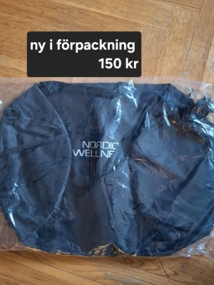 Svart gymväska från Nordic Wellness - Säljer en svart gympåse från Nordic Wellness med dragsko och mesh-detaljer på sidorna. Perfekt för att bära träningskläder eller skor till gymmet. Tillverkad i slitstarkt syntetmaterial och har logga framtill.