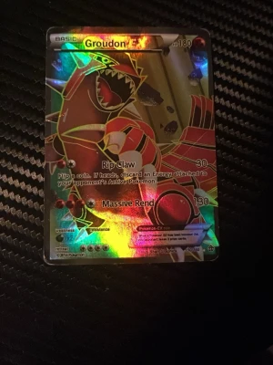 Pokémonkort Groudon EX Full Art - Säljer ett Pokémonkort Groudon EX Full Art med holografisk yta. Kortet har färger i rött, gult och svart med coola effekter och visar Groudon i en kraftfull pose. Perfekt för samlare eller Pokémonfans som vill utöka sin kortsamling.