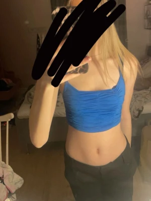 Blå croppad linnetopp - Säljer en blå croppad linnetopp med rynkade detaljer framtill och smala axelband. Toppen har en tight passform och är perfekt för dig som gillar att sticka ut med färg. Materialet känns mjukt och stretchigt, vilket gör den bekväm att bära.