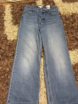 Blåa wide leg jeans från H&M - Ett par blåa jeans från H&M med rak och bred passform. Jeansen har klassisk femficksdesign, hög midja och är tillverkade i denim. Perfekta för en avslappnad och trendig stil.
