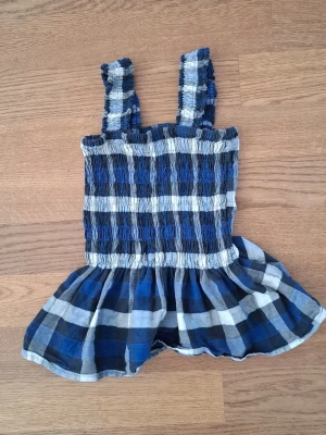 Blårutig volang linnetopp - Söt linnetopp med breda axelband och volang nertill. Toppen har ett rutigt mönster i blått, vitt och svart, samt formar sig väl efter kroppen. Oanvänd och köpt i nytt skick från Prag Copenhagen