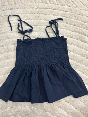 Mörkblå smockad linnetopp från SHEIN - Supersöt mörkblå linnetopp från SHEIN med smockad överdel och volang nedtill. Toppen har tunna axelband med knyt och en lätt rynkad kant upptill. Perfekt till sommaren och enkel att styla med jeans eller kjol.