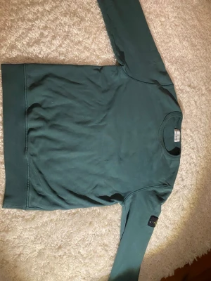 Mörkgrön crewneck sweatshirt - Säljer en mörkgrön crewneck sweatshirt från STONE ISLAND Tröjan har en klassisk rak passform, långa ärmar och ribbade muddar. På vänster ärm sitter det ikoniska STONE ISLAND. Tillverkad i mjuk bomullsblandning för skön känsla.