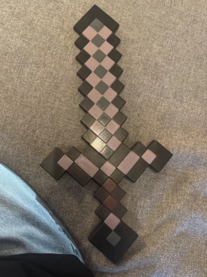 Minecraft-inspirerat svärd i plast - Säljer ett svart och grått Minecraft-inspirerat svärd i plast. Svärdet har en pixlad design med rutmönster och är perfekt som accessoar till cosplay eller maskerad, eller en leksak. Som det är till för. Lätt att bära och ger en autentisk gamingkänsla till din outfit.