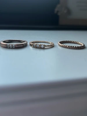 Tre tunna ringar med stenar - Säljer tre stilrena ringar i olika metalltoner. Två av ringarna har små gnistrande stenar infattade framtill, medan den tredje har en pärlad struktur runt hela ringen. Perfekta att bära tillsammans eller var för sig för en trendig look.