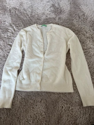 Vit basic kofta med rund hals - Klassisk vit kofta med v ringad halsringning och knappar framtill. Långärmad modell med ribbade muddar vid ärmslut och nederkant. Perfekt att matcha med olika outfits för en enkel och stilren look.