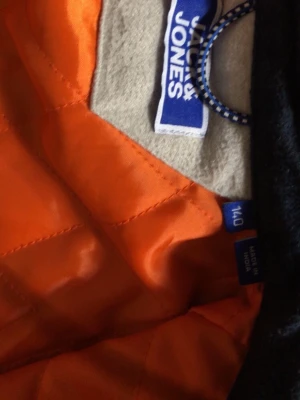 Mörkblå overshirt från Jack & Jones - Snygg mörkblå overshirt från Jack & Jones med orange quiltat foder. Klassisk skjortkrage och långa ärmar med knapp vid ärmslut. Perfekt lager på lager-plagg med kontrastfärgad insida som sticker ut. Tillverkad i ett tåligt material.