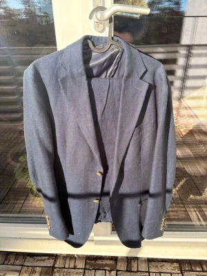 Marinblå linnekostym från John Henric - Snygg marinblå linnekostym från John Henric med klassisk passform och två guldknappar framtill, kavajen är storlek 46, byxorna 50, bra för någon som är lång och smal. Liten defekt i armhålan där sömmen lossnat, men inget som märks från utsidan eller gör skillnad i bekvämlighet.    Det går att köpa de separat, skriv i Dm. 