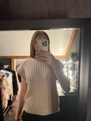 Beige stickad kortärmad topp - Säljer en beige stickad topp med korta ärmar och rund hals. Tröjan har ett luftigt, ribbat mönster. Knappt använd