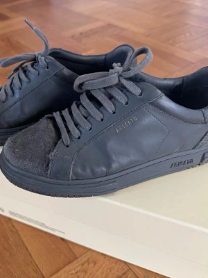 Gråa sneakers från Axel Arigato - Snygga gråa sneakers från Axel Arigato i läder med mockadetaljer på tån och hälen. Klassisk låg modell med matchande gråa snören. Perfekta för en clean och stilren look.
