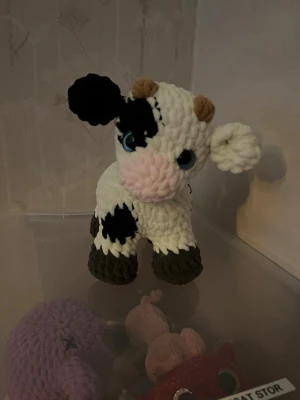 Virkad mjukisko  - Söt handvirkad mjukisko med vita och svarta fläckar, rosa mule, bruna horn och stora blå glittriga ögon. Tillverkad i mjukt garn och har gråa ben. Perfekt som dekoration eller gosedjur. Virkat av mig. 