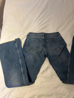 Blå raka jeans med fem fickor - Säljer ett par klassiska blå jeans med rak passform och fem fickor. Jeansen har låg midja och är tillverkade i ett slitstarkt denimtyg. Perfekta för en avslappnad och trendig look.
