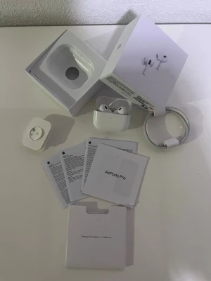 Apple AirPods Pro trådlösa hörlurar - Säljer ett par vita Apple AirPods Pro med laddningsetui, originalkartong, laddkabel och manualer. Hörlurarna är kompakta, har silikonproppar och är tillverkade i blank plast. Perfekta för dig som vill ha grymt ljud och smidig anslutning till Apple-enheter.