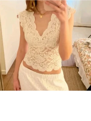 Vit spetsblus med v-ringning - Söt vit blus i spets med v-ringning och korta ärmar. Toppen har fina volangdetaljer längs kanterna och är lätt genomskinlig för en romantisk look. Perfekt att styla med kjol eller jeans.