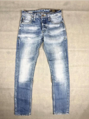 Jack & Jones Jeans - Säljer ett par ljusblå jeans med slitna och tvättade detaljer. Jeansen har fem fickor, normal midja och smal passform. Materialet är klassisk denim i bomull och de har snygga slitningar på låren och knäna för en trendig look.