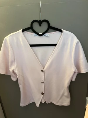 Ljusrosa v-ringad topp med knappar - Söt ljusrosa topp från lager med v-ringning och korta ärmar. Toppen har tre dekorativa knappar framtill och är croppad i modellen. . Varit efterfrågad på TikTok!!!!!!