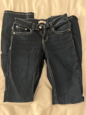 Mörkblå jeans med kontrastsömmar - Mörkblå jeans från Perfect Jeans med vita kontrastsömmar och femficksmodell. Baktill finns två fickor med lock och silverfärgade knappar. Klassisk passform och tillverkade i denim. Perfekta för en trendig och avslappnad stil.