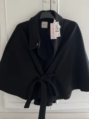 Svart cape med knytband Gina Tricot - Säljer min helt oanvända kappa från Gina. Storlek XS/S men passar även de som har storlek M. 