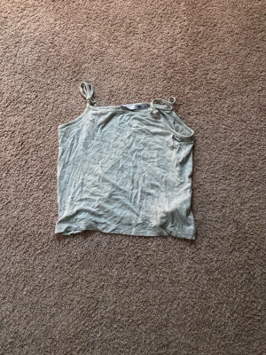 Ljusgrå linnetopp med knyt - Säljer en ljusgrå linnetopp från 157 med tunna axelband som knyts upptill. Toppen är ärmlös och har en enkel, rak passform i mjukt bomullsmaterial. Perfekt för varma dagar eller att styla lager på lager.