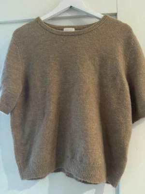Beige stickad tröja från H&M - Stickad tröja från H&M i mjuk beige ton. Tröjan har korta ärmar, rund halsringning och ribbade muddar vid ärmslut och nederkant. Perfekt för lager på lager och enkel att matcha med olika stilar.