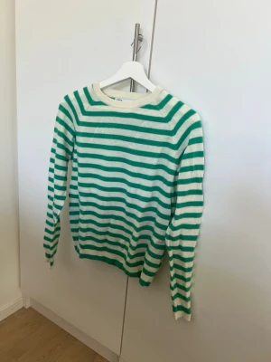 Randig stickad tröja från Zara - Snygg stickad tröja från Zara med gröna och vita horisontella ränder. Tröjan har rund halsringning och långa ärmar. Perfekt för dig som gillar en fräsch och trendig look. Materialet känns mjukt och bekvämt.