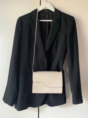 ATP Atelier  - Ny ATP Atelier-väska i benvit med svart trim – stilren och tidlös med en fin kontrast. Axelbandet kan användas på två sätt, enkelt eller dubbelt. Lika snygg till en helvit look som till svart, och enkel att matcha oavsett tillfälle. Kommer så klart med dustbag.