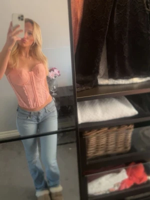 Rosa spetskorsett med bygel - Säljer en snygg rosa korsett med bygel och vadderade kupor. Korsetten har spetsdetaljer och markerade sömmar framtill som ger en feminin siluett. Axelbandslös design och hakknäppning bak. Perfekt att styla till jeans eller kjol.