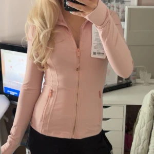 Ljusrosa define jacket lululemon - Snygg ljusrosa define jacket från lululemon med figurnära passform. Tröjan har långa ärmar, dragkedja framtill och två fickor med dragkedja. Tillverkad i ett stretchigt och mjukt material som passar perfekt till träning. Lappen sitter kvar och är oanvänd! Storlek 4 och modellen är Luon!💕