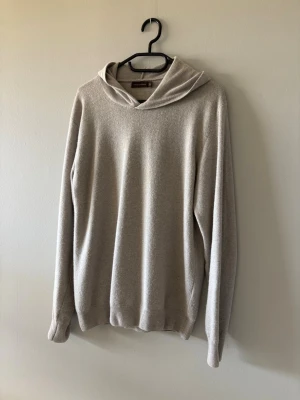 Beige hoodie från Oscar Jacobson  - Snygg beige hoodie från Oscar Jacobson i mjukt och tunt material. Hoodien har en enkel och stilren design med ribbade muddar vid ärmslut och nederkant. Perfekt för dig som gillar en clean och avslappnad look. Färg beige/grå. Storlek S men kan passa M