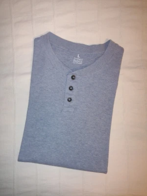 Grå kortärmad farfarströja/t-shirt från Our Best Basics, 100% bomull - En kortärmad, mjuk och stretchig farfarsröja i en fin ljusblå/blågrå färg. Our Best Basics, KappAhl. Storlek L, 100% bomull. Bara använd någon enstaka gång och i så gott som nyskick.